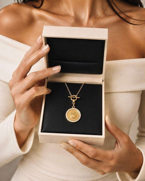 An open jewelry box holding the gold Fudge coin necklace