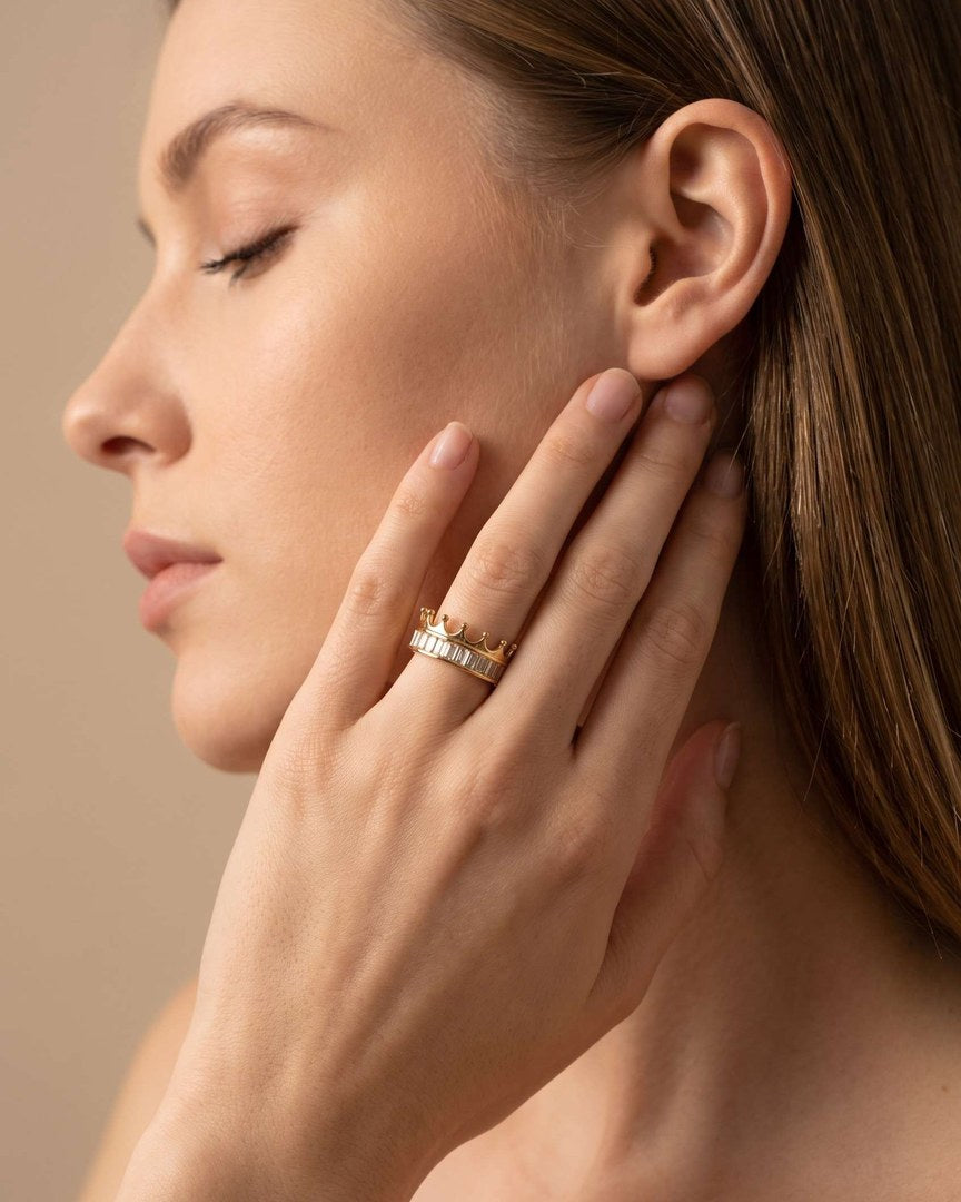A hand over one eye, wearing the gold crown ring
