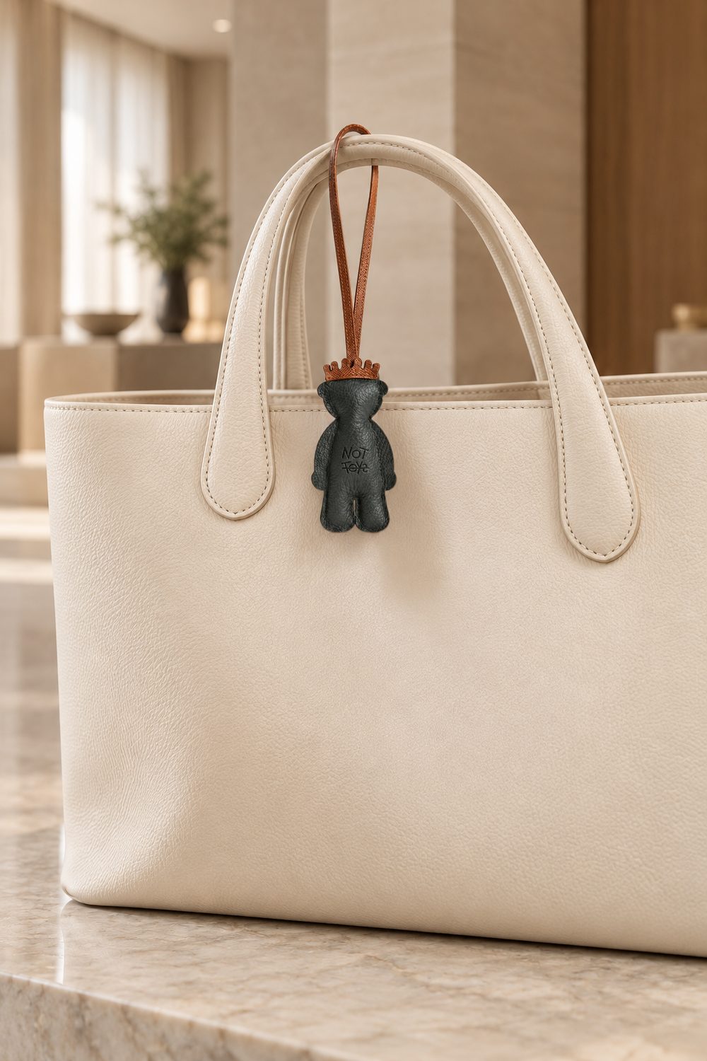 The Fudge charm hanging from a cream leather tote