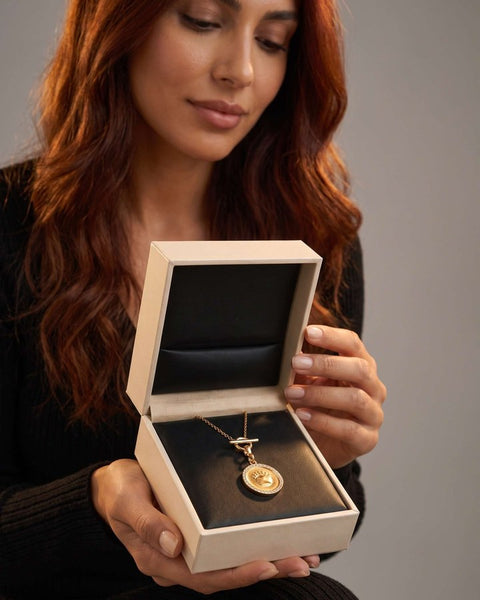 A woman holding an open box with the Fudge coin necklace